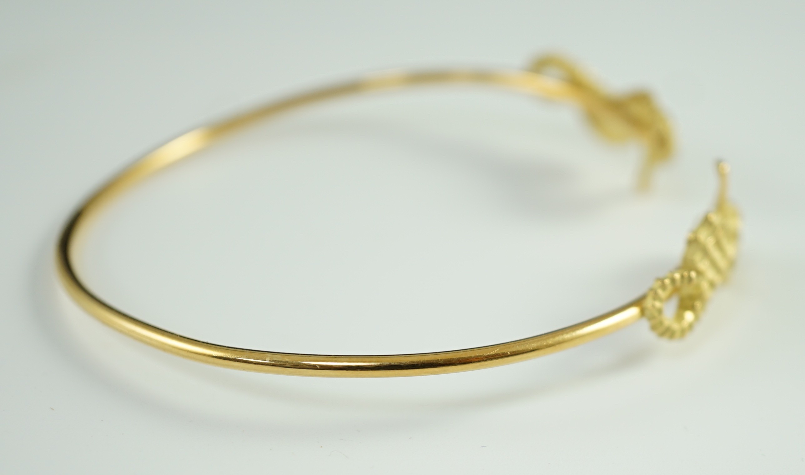 A modern gold and diamond chip set open work bangle, each terminal modelled as a seahorse with diamond chip eye